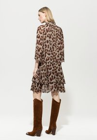 Leopardenmuster, gestuftes Kleid, leichtes Material, drei Viertelärmel. Braune Wildleder-Stiefel, knielang mit Blockabsatz und metallischen Akzenten.