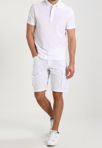 Polo shirt blanc avec un col court et un logo brodé, accompagné de shorts cargo blancs avec plusieurs poches et une coupe classique.