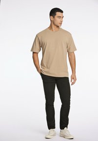 Beige T-shirt met korte mouwen en een ronde halslijn, gecombineerd met zwarte slim-fit jeans en witte sneakers. Eenvoudig ontwerp, gladde stof.