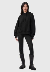 Svart överdimensionerad hoodie med en framficka, justerbar dragsko på huvan och ribbade ärmslut, kombinerad med svarta leggings och knähöga stövlar.