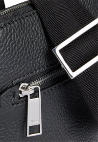 Czarna, teksturowana skórzana torba z metalowym zamkiem błyskawicznym i prostokątnym uchwytem, uzupełniona trwałym czarnym paskiem i wypolerowanymi akcentami hardware.