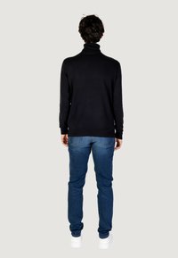 Pullover a collo alto nero con maniche lunghe, abbinato a jeans blu e sneakers bianche. Il tessuto appare liscio e aderente.