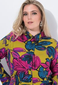 Krátký rukáv, košile na knoflíky v živé žluté barvě s velkými růžovými a modrými vzory listů. Obsahuje klasický límec a černé knoflíky.