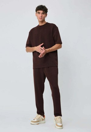 T-shirt marron à manches courtes et pantalon assorti à coupe décontractée. Baskets avec des accents beige et orange. Texture de tissu lisse et design décontracté.