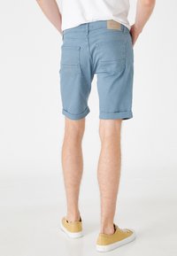 Shorts de denim azul claro con puños enrollados, cinco bolsillos y una etiqueta en la cinturilla trasera. El material parece suave y tiene una textura lisa.