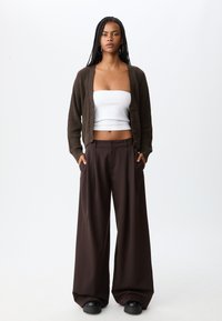 Bruin gebreid cardigans met knopen, witte strapless top en brede bruine broeken. Zwarte platform schoenen maken de look compleet. Eenvoudig, modern ontwerp.