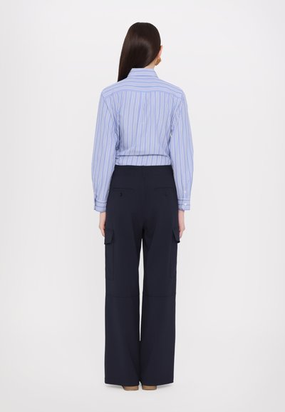Chemise à rayures bleu clair et blanche, associée à un pantalon cargo ample bleu marine avec poches latérales et une texture lisse.