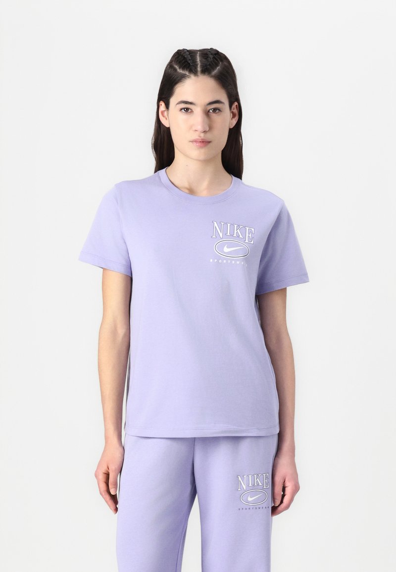 Šviesiai violetinė medvilninė marškinėliai su apvalia kaklo iškirpte ir trumpomis rankovėmis, ant krūtinės atspaustas įrašas "NIKE" ir logotipas. Derinama su atitinkamomis kelnėmis.