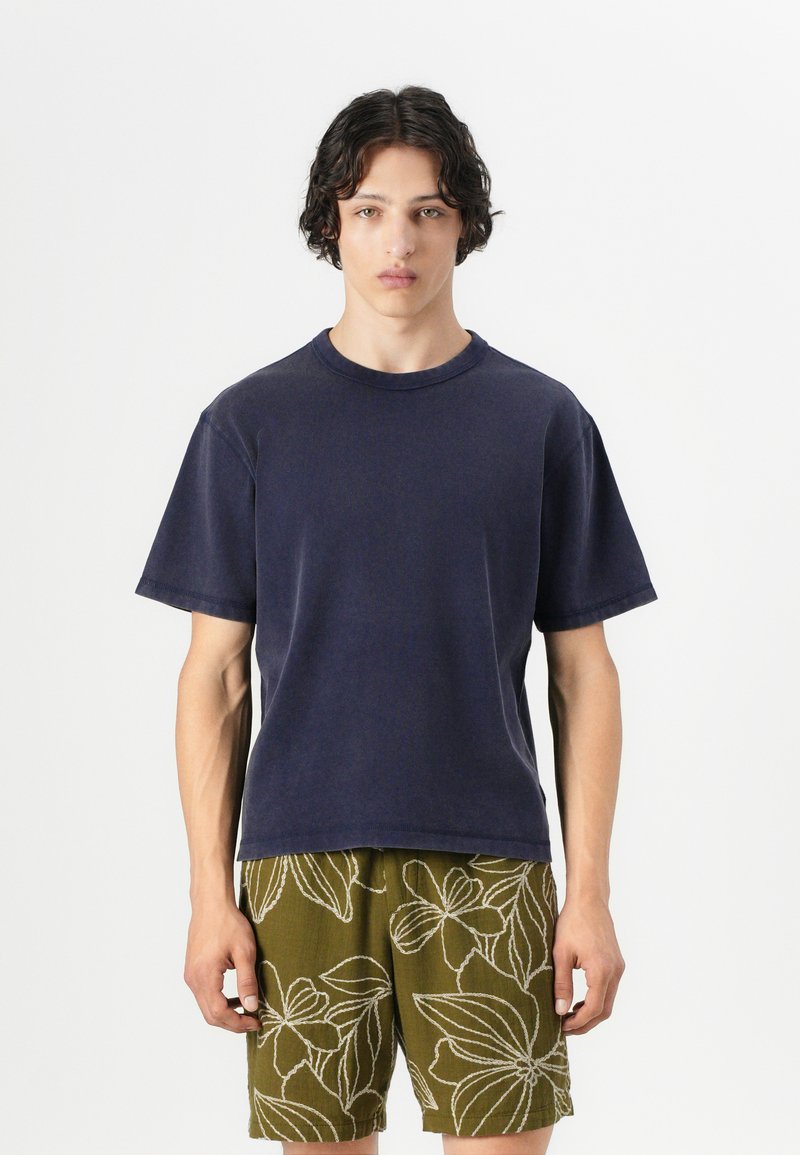 Navy cotton t-shirt with a crew neck and short sleeves, paired with olive green shorts featuring white floral patterns.