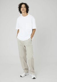 T-shirt blanc à manches courtes avec une poche poitrine, associé à un pantalon en lin beige clair ample, et des chaussures de sport blanches.