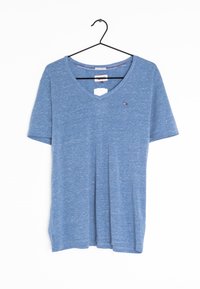 Lyseblå bomulds T-shirt med v-hals, korte ærmer, blød tekstur og et lille logo på venstre bryst. Hængende fra en sort krog.