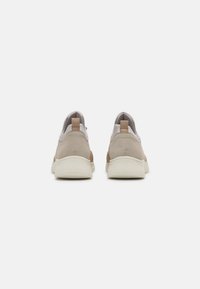 Light beige sneakers with a smooth, textured finish. Features a cream rubber sole, back pull tab, and subtle brown accents.