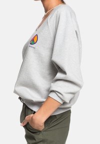 Sudadera gris de corte holgado, con cuello en V y puños de canalé. Presenta un logo colorido de símbolo de paz y una textura de tela suave.