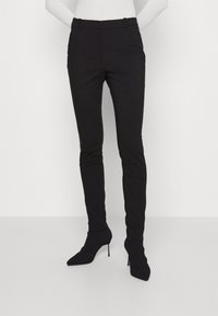 Zwarte slim-fit broeken van een gladde stof, met een middelhoge taille en voorzakken, gecombineerd met puntige zwarte enkellaarsjes.