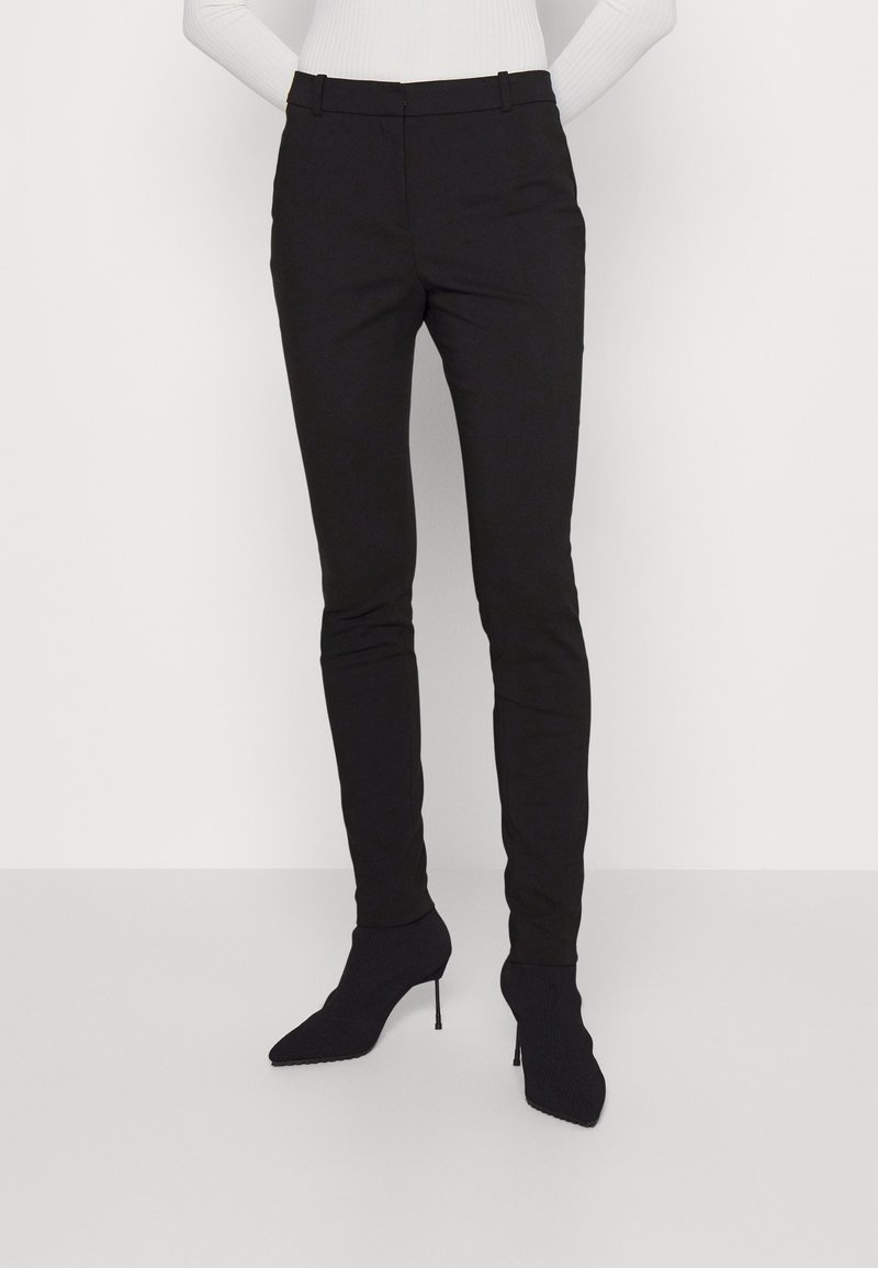 Zwarte slim-fit broeken van een gladde stof, met een middelhoge taille en voorzakken, gecombineerd met puntige zwarte enkellaarsjes.