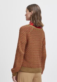 Pull en tricot avec un motif brun et rouge, au design texturé et épais, encolure ronde et bords-côtes aux poignets et à l'ourlet.