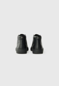 Zapatillas altas de piel negra con acabado texturizado, suelas de caucho planas y acentos mínimos en la parte trasera. Vista desde atrás.