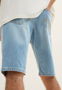 Pantalones cortos de mezclilla en azul claro, con detalles de costura visibles y una textura ligeramente desgastada. Con corte recto y bolsillos laterales.