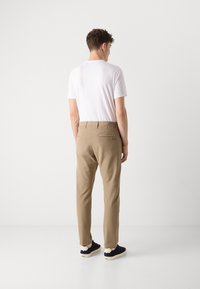 Pantaloni bej cu o croială ajustată, dotati cu buzunare la spate și un logo. Purtați cu un tricou alb și teniși negri. Textură netedă.