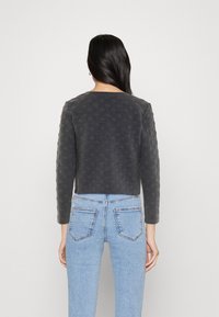 Suéter gris recortado con un patrón texturizado, mangas largas y escote redondo, combinado con unos jeans de tiro alto en azul claro.