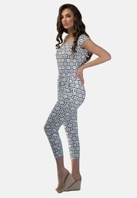 Biały kombinezon z czarnymi geometrycznymi wzorami, krótki rękaw, dopasowany krój i ścięte nogawki, zestawiony z sandałami na plecionych obcasach.