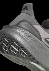 Grå atletisk sko med en textureret overdel, der har en polstret sål og en mønstret ydersål, mærket "ULTRABOOST" nær hælen.