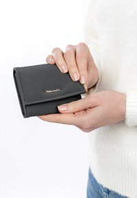 Zwarte leren portemonnee met een opklapbaar ontwerp, voorzien van een gouden logo, vastgehouden in handen en toont een gladde textuur en een compact formaat.