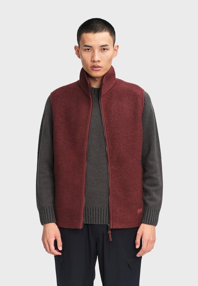 Bordeaux fleece vest med høj krave og lynlås, båret over en mørkegrå struktureret sweater. Har en lige pasform og ingen ærmer.