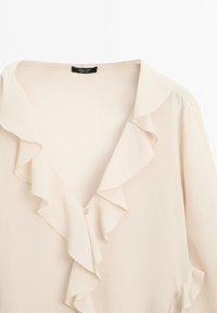 Blusa rosa con colletto arricciato e dettagli con bottoni. Realizzata in tessuto leggero, presenta una texture liscia e una vestibilità comoda.
