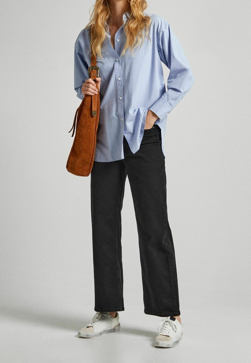 Chemise boutonnée bleu clair, pantalon noir à jambes larges, baskets blanches et sac à bandoulière en daim marron. Tissu lisse avec une coupe décontractée.