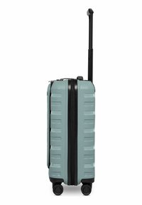 Valise rigide bleu clair avec surface texturée, fermeture éclair noire, quatre roues noires, et poignée télescopique noire étendue, vue de côté.