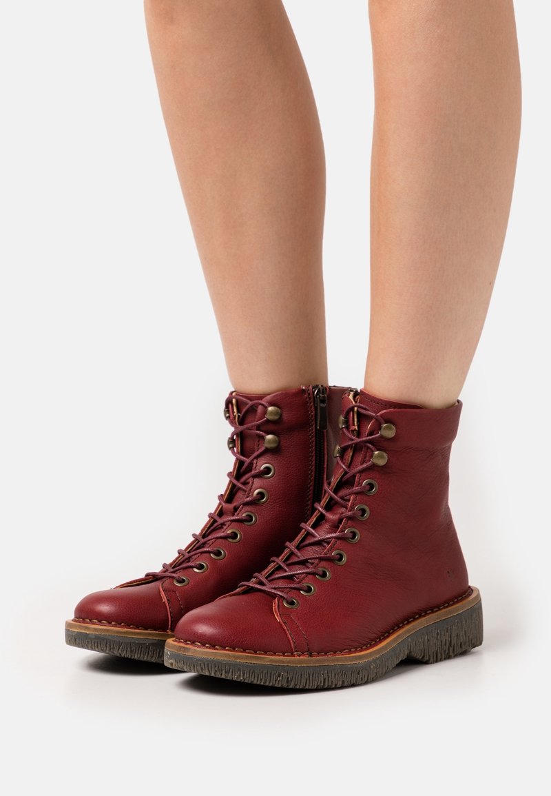Botines de cuero rojo hasta el tobillo con puntera redondeada, suela marrón texturizada, cordones en la parte delantera y cremallera lateral. Presenta ojales de metal y costura en contraste.
