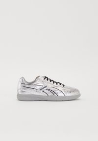 Srebrna atletska čevlja z teksturirano površino, črnimi poudarki in vezalkami. Ima zaobljen prst in sivo gumijasto podplat.