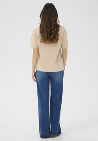 Beige bomulds T-shirt med afslappet pasform og korte ærmer, parret med løse blå denimjeans, set fra ryggen.