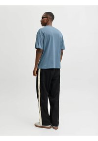 Niebieska, oversize'owa koszulka z krótkim rękawem, w połączeniu z czarnymi spodniami z kremowym bocznym pasem. Całość dopełniają casualowe obuwie.