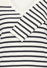 Pull rayé avec un col en V, présentant des rayures bleu marine sur un fond crème, fabriqué en maille douce. Accentué par des poignets côtelés.