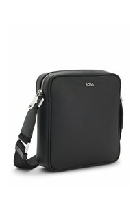 Sac bandoulière rectangulaire noir avec sangle réglable, fermeture éclair argentée et petit logo "BOSS" à l'avant.