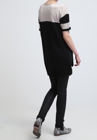 Tunique en tricot avec une partie inférieure noire et un haut gris clair. Comprend des manches courtes, une coupe décontractée et un tissu texturé. Associée à un jean noir et des chaussures à motifs.