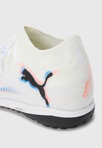 Białe buty sportowe Puma z czarnym logo, plecionym kołnierzem wokół kostki, teksturowaną czarną podeszwą oraz czerwonym napisem "Play Free Future" na pięcie.