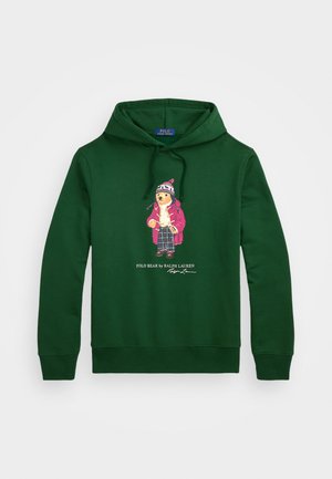 Sudadera de algodón verde con un gráfico de un oso vestido, con un gran bolsillo frontal y capucha con cordón. Texto del logo debajo del diseño.