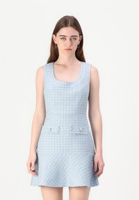 Robe en tweed bleu clair avec un décolleté rond, sans manches, et deux poches avant ornées de boutons décoratifs. Fini texturé.