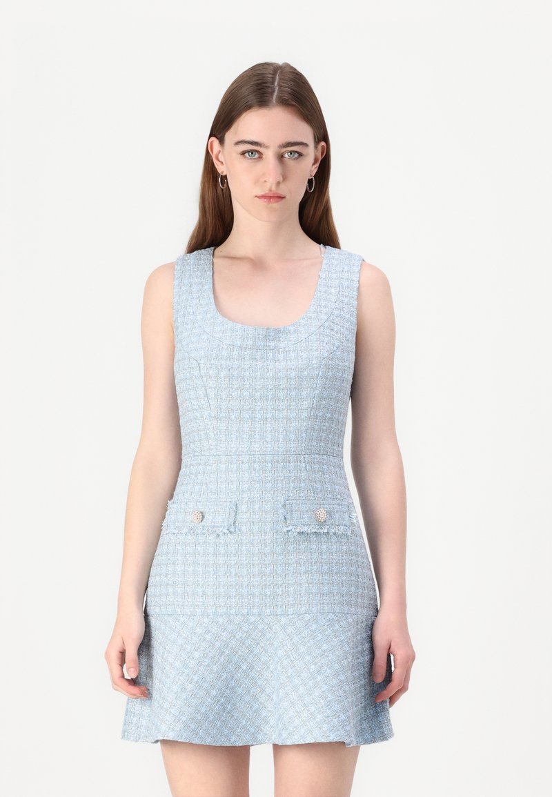 Robe en tweed bleu clair avec un décolleté rond, sans manches, et deux poches avant ornées de boutons décoratifs. Fini texturé.