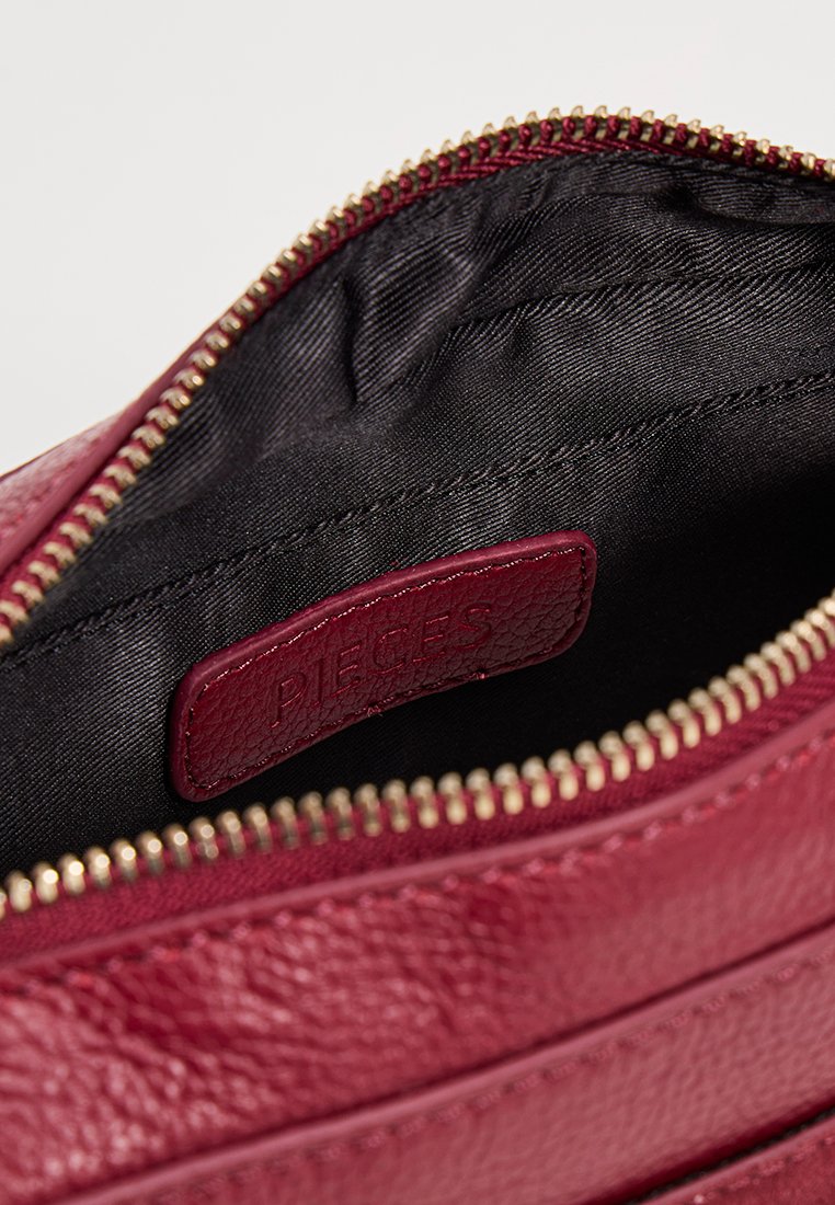 Otwarta ciemnoróżowa skórzana torba z złotym zamkiem i czarnym materiałowym wnętrzem, na którym widoczna jest skórzana metka z wytłoczonym napisem "PIECES".