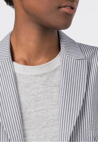 Pasiakowana marynarka z dopasowanym kołnierzem, w kolorze białym i granatowym. Miękki, biali koszula pod spodem. Skupienie na czystych liniach i prostocie materiału.