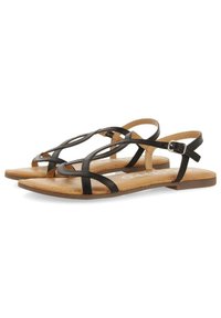Sandalias planas de cuero negro con correas entrecruzadas y hebilla en el tobillo. Plantilla de color marrón claro con una textura suave; diseño minimalista.