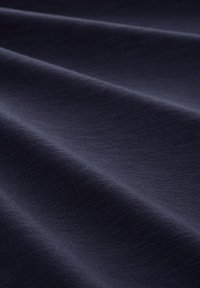Marineblauwe stof met een zachte, gestructureerde oppervlakte, die subtiele diagonale lijnen en plooien toont, en er soepel en flexibel uitziet.