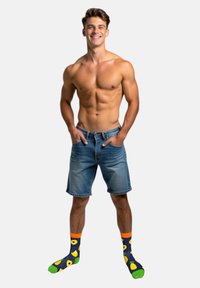 Shorts en denim, bleu clair, coupe décontractée. Chaussettes colorées avec des motifs de fruits : base bleu foncé, accents verts et oranges, présentant des designs d'avocat et d'ananas.