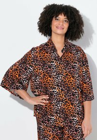Kortærmet bluse i orange og sort leopardprint, med en knaplukket krave og løs pasform. Glat stof med en blank overflade.