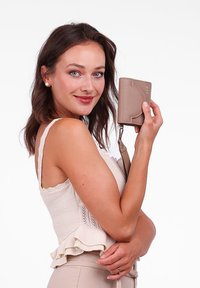 Beige wallet made of textured material, featuring a circular detail and a wrist strap, held by a person with a light knit top.