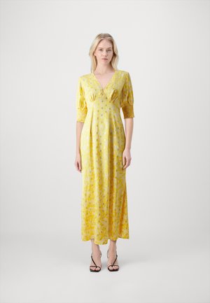 Yellow floral maxi dress with a deep V-neck, short puff sleeves, and smocked shoulders. Worn with black strappy sandals.